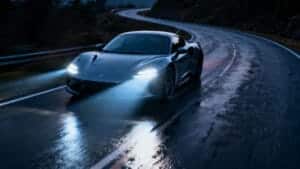 Современный автомобиль едет ночью, его мощные светодиодные фары освещают мокрую дорогу впереди.